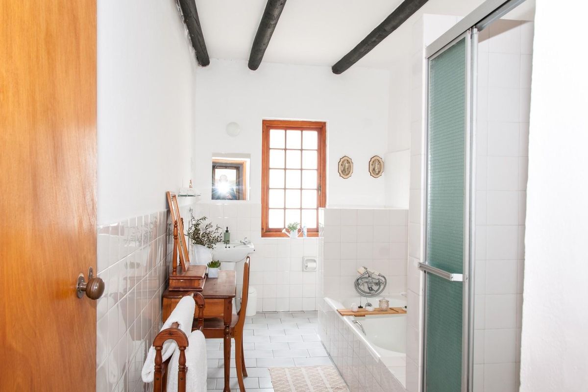 A rustic bathroom featuring exposed timber ceiling beams, a built-in bathtub, a separate shower enclosure, and tiled flooring.