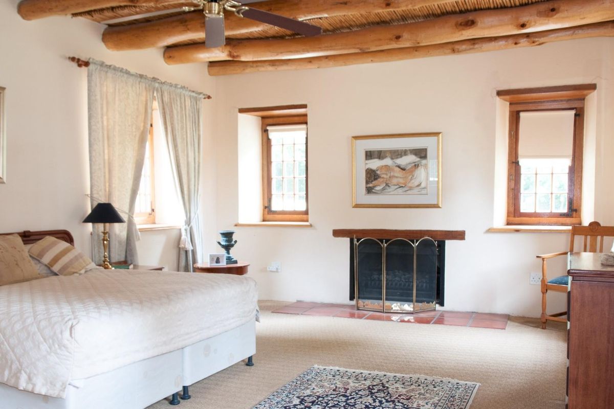 Spacious bedroom featuring exposed timber ceiling beams, a built-in fireplace with a tiled hearth, and traditional wooden window frames.