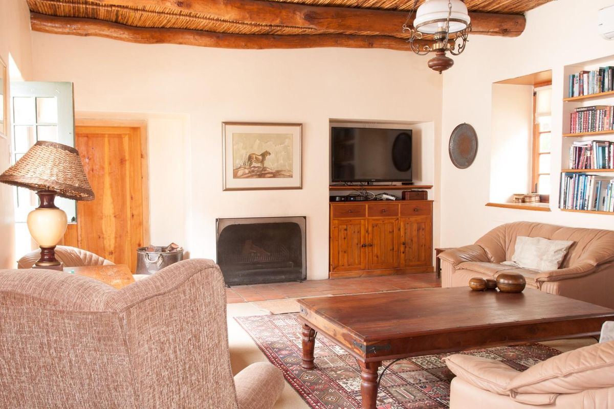 A rustic living room featuring a traditional fireplace, exposed timber beam ceiling with thatch detailing, and built-in shelving.