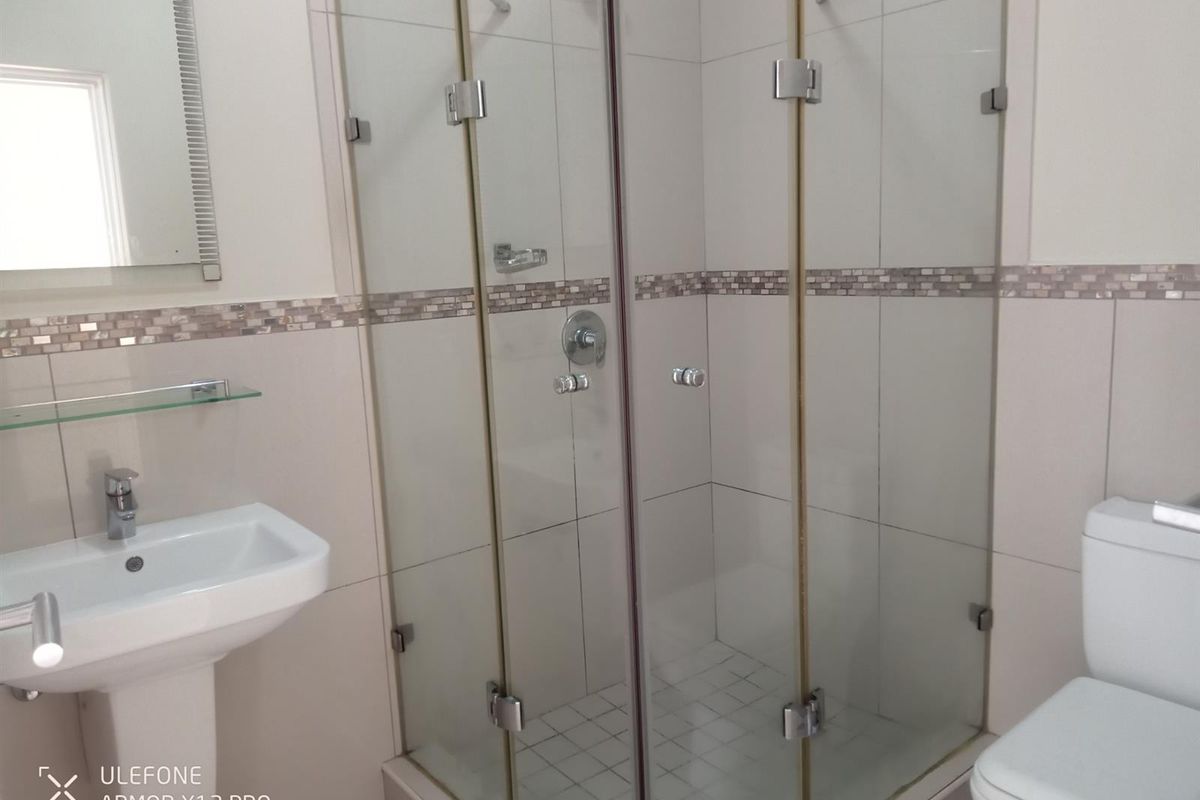 A clean, modern bathroom featuring a glass-enclosed shower, pedestal basin, and a standard toilet with neutral wall tiling.