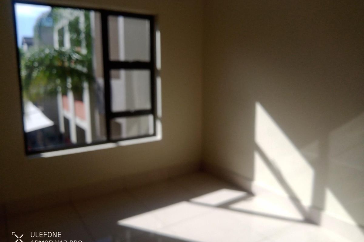 A bright, empty bedroom featuring tiled flooring and a large window allowing natural light to enter the space.