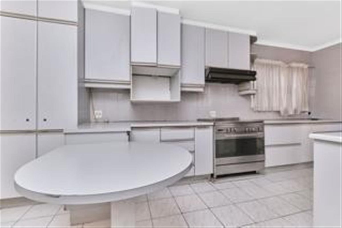 A functional kitchen featuring light-toned cabinetry, a stainless steel freestanding oven with extractor fan, and tiled flooring.