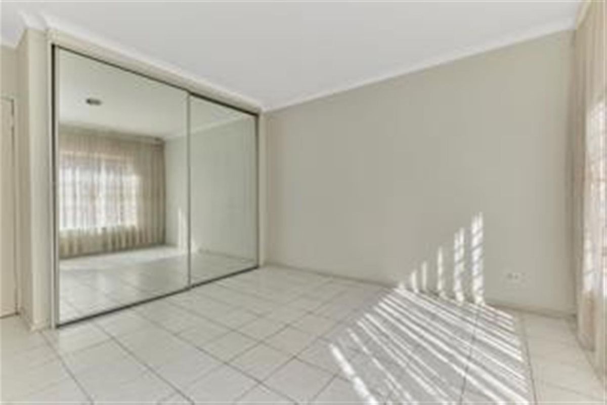 A bright, empty bedroom featuring large mirrored sliding built-in wardrobes and neutral tiled flooring, offering a clean and versatile living space.