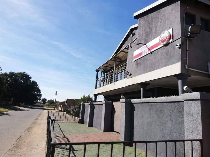 Exterior view of a multi-level commercial or residential property featuring a balcony, boundary wall, and paved entrance area along the street.
