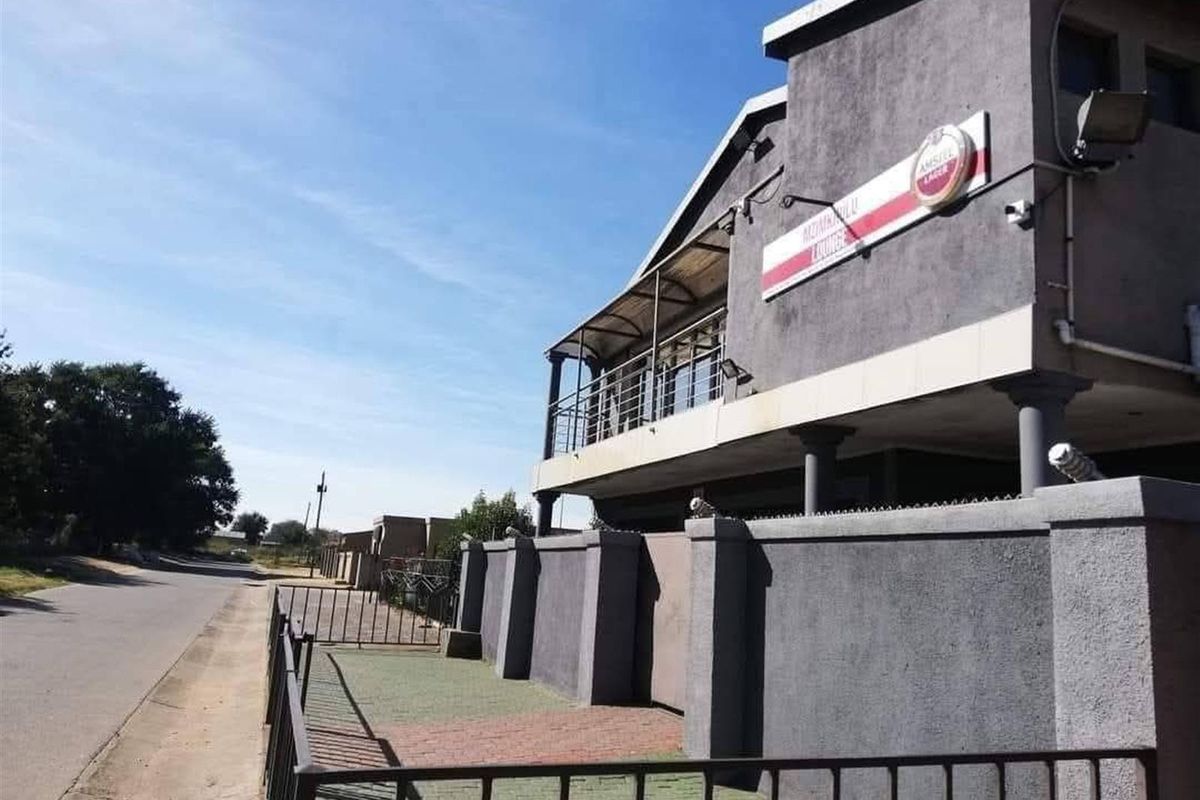 Exterior view of a multi-level commercial or residential property featuring a balcony, boundary wall, and paved entrance area along the street.