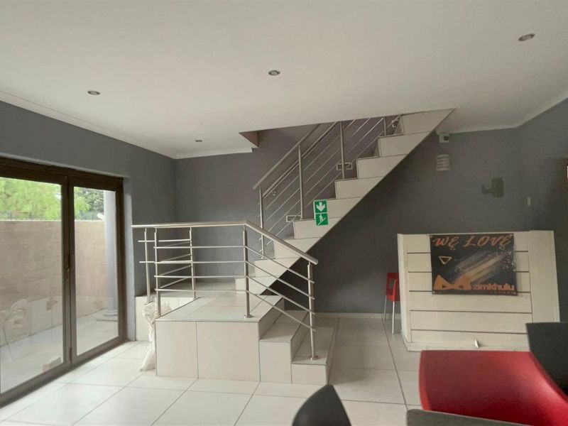 Open plan living area featuring a modern staircase with stainless steel balustrades, tiled flooring, and large sliding glass doors leading to the exterior.