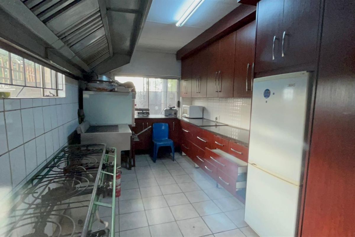 A functional kitchen featuring dark wood cabinetry, tiled flooring, and an industrial-style extractor hood, offering potential for modernization and layout optimization.