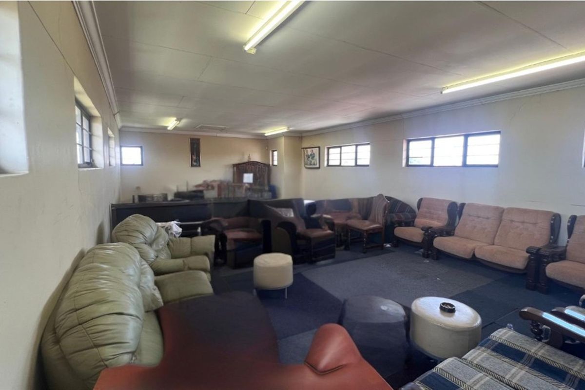 Spacious living area featuring carpeted flooring, multiple steel-framed windows, and fluorescent lighting, offering a large footprint for potential renovation and modernization.