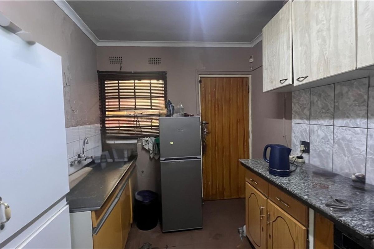 A functional kitchen featuring built-in cabinetry, laminate countertops, and a tiled backsplash, currently requiring cosmetic updates and wall repairs.