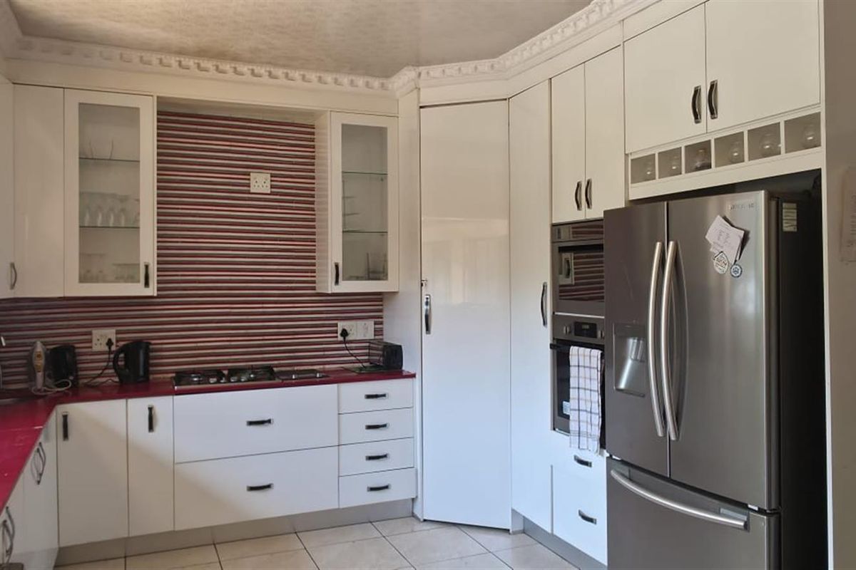 A functional kitchen featuring white cabinetry, integrated oven, gas hob, and a double sink with a contrasting red countertop.