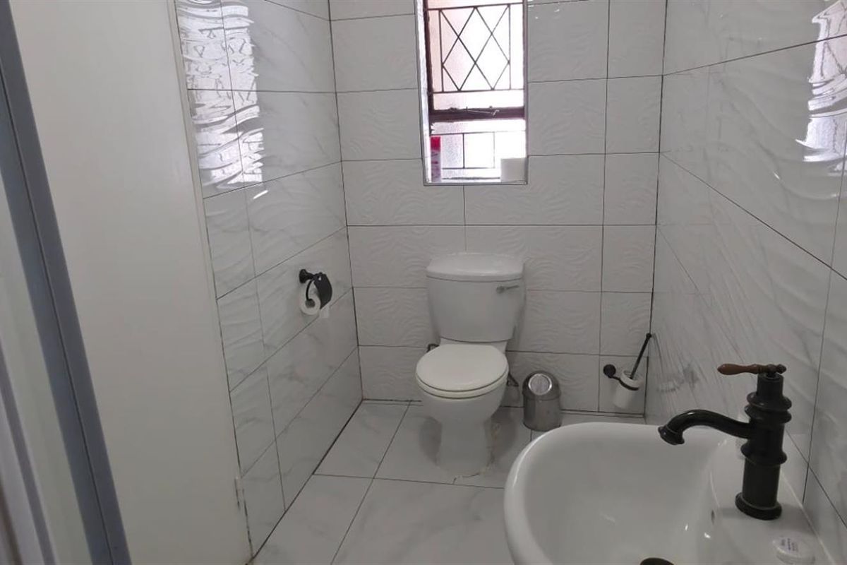 A compact guest bathroom featuring white wall tiles, a standard toilet, and a small pedestal basin with a vintage-style faucet.