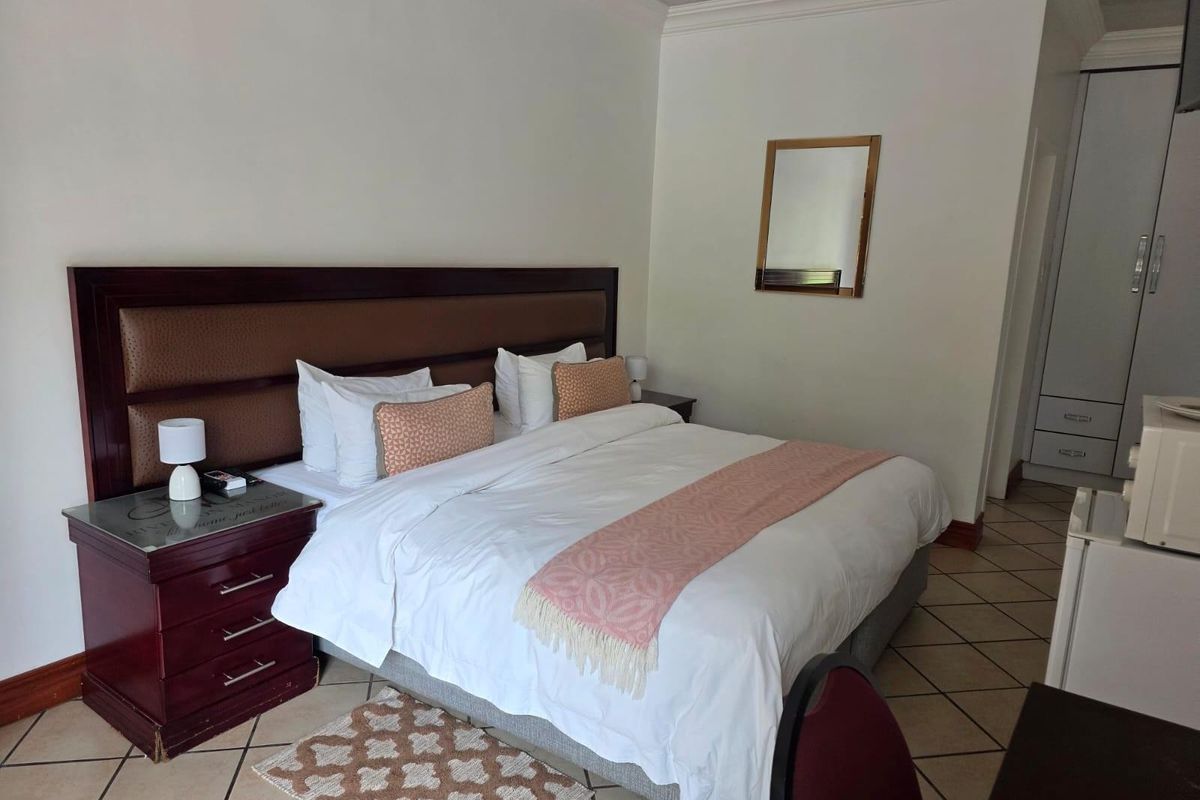A guest bedroom featuring tiled flooring, built-in wardrobe storage, and a large upholstered headboard.