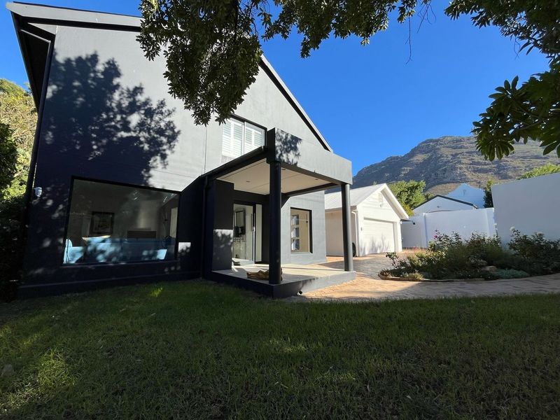 A modern dark-painted rear exterior featuring a covered patio, paved driveway, detached garage, and well-maintained garden with mountain views.