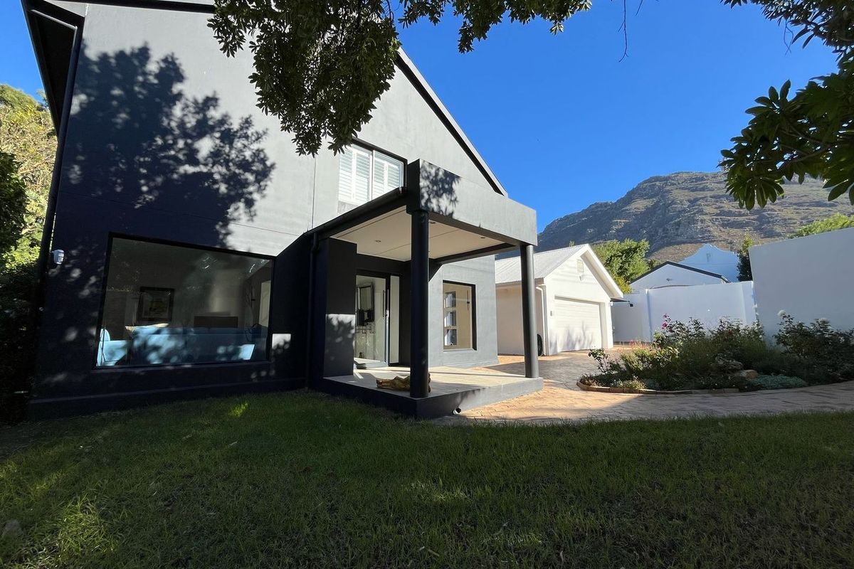 A modern dark-painted rear exterior featuring a covered patio, paved driveway, detached garage, and well-maintained garden with mountain views.