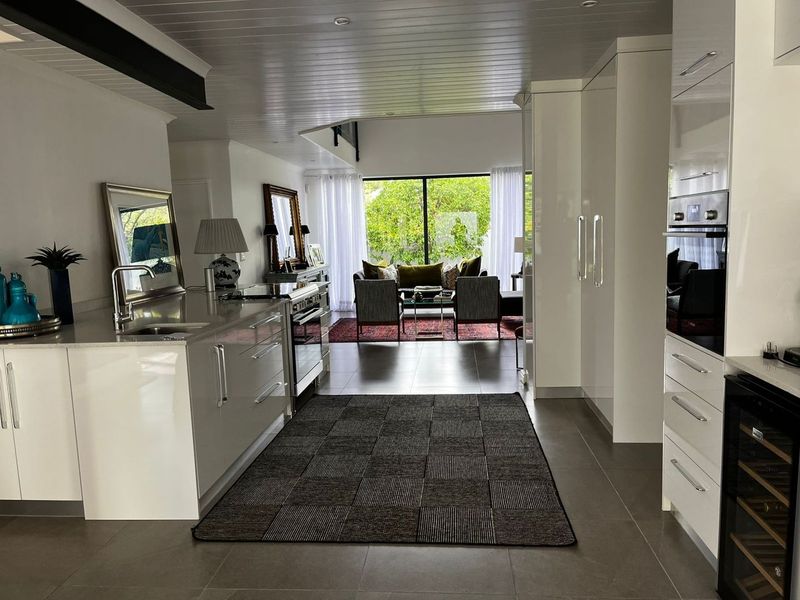 Modern open-plan kitchen and living area featuring sleek cabinetry, stone countertops, integrated appliances, and large glass doors leading to the garden.