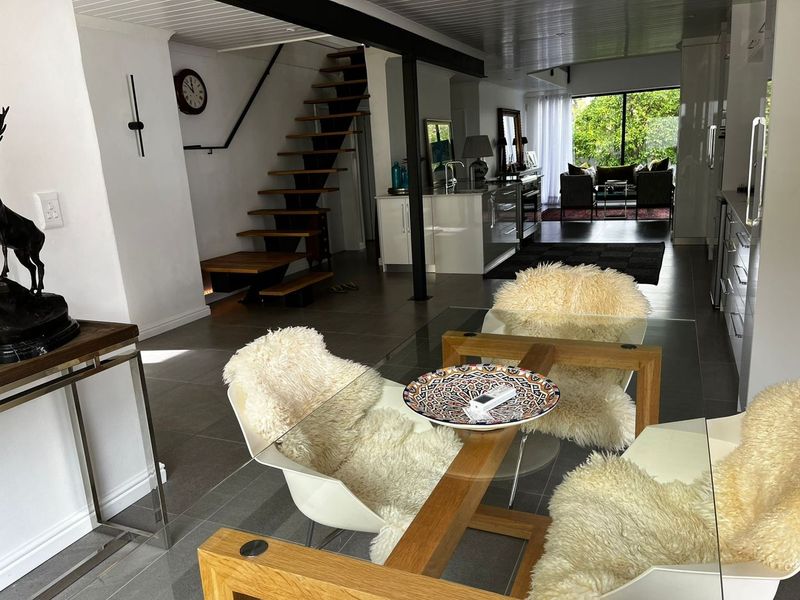Spacious open-plan living area featuring a modern open-tread staircase, sleek tiled flooring, and seamless flow to the rear garden through large sliding glass doors.