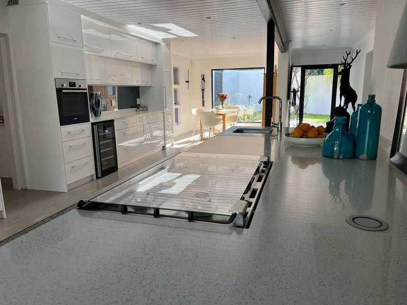Modern open-plan kitchen featuring a large stone island with integrated cooktop, sleek white cabinetry, and seamless flow to the outdoor dining area.
