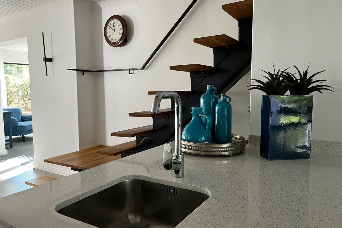 Modern kitchen area featuring a stone countertop with an undermount sink, adjacent to a contemporary floating staircase with a metal handrail.