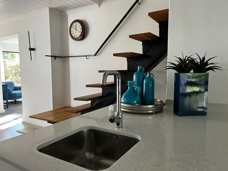Modern kitchen area featuring a stone countertop with an undermount sink, adjacent to a contemporary floating staircase with a metal handrail.