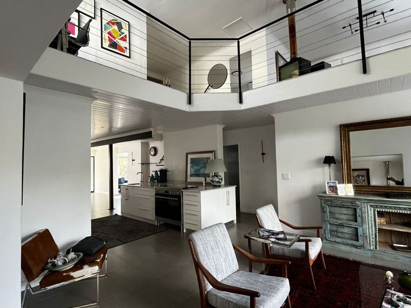 Spacious open-plan living area featuring a modern kitchen island, mezzanine level with metal balustrade, and a prominent wood-burning fireplace.
