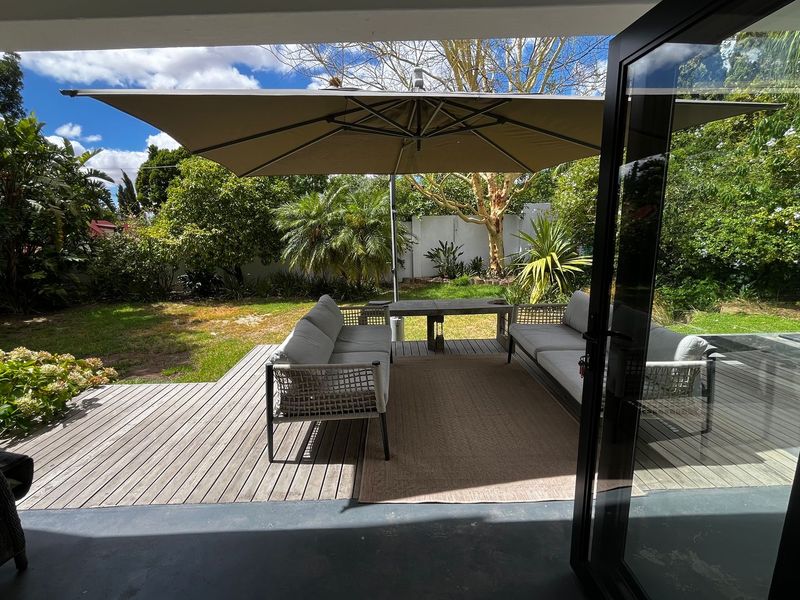 A covered timber deck patio featuring black aluminium framed glass doors, providing seamless indoor-outdoor flow to the landscaped garden.