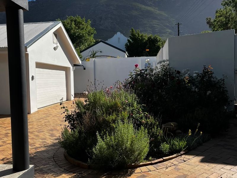 Front exterior view featuring a brick paved driveway, a garage, and a landscaped garden bed set against a mountain backdrop.