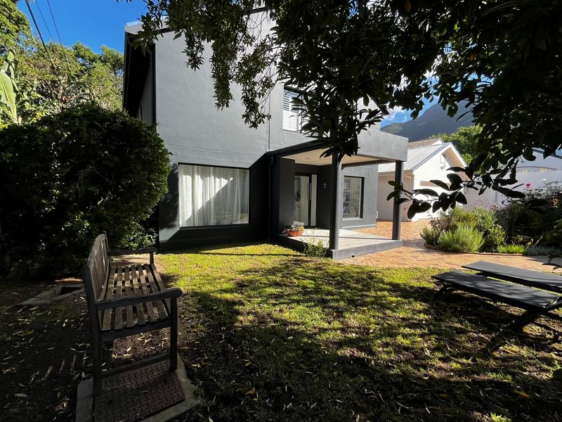 A well-maintained rear exterior view featuring a dark-painted facade, a covered patio area, and a landscaped garden with paved terrace.