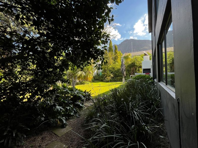 A lush, well-maintained rear garden featuring a stone pathway, mature landscaping, and a built-in outdoor fireplace, offering a private and serene outdoor space.