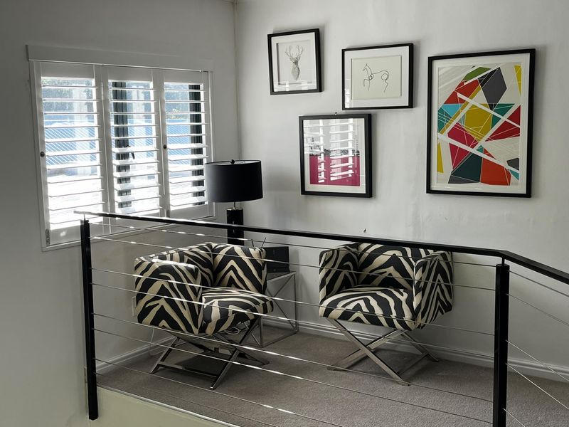 A bright landing or hallway area featuring modern metal cable balustrading, carpeted flooring, and plantation shutters on the window.