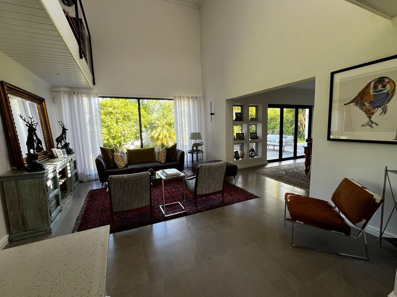Spacious double-volume living area featuring large windows, tiled floors, and built-in display shelving, offering a bright and airy atmosphere with seamless flow to the outdoors.