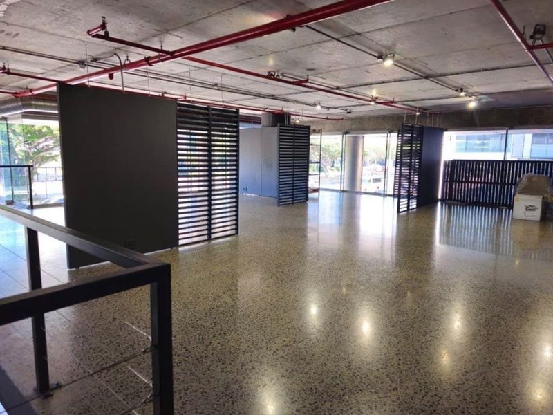 Spacious open-plan retail or office area featuring polished concrete floors, exposed industrial ceilings with fire sprinklers, and large glass windows providing ample natural light.