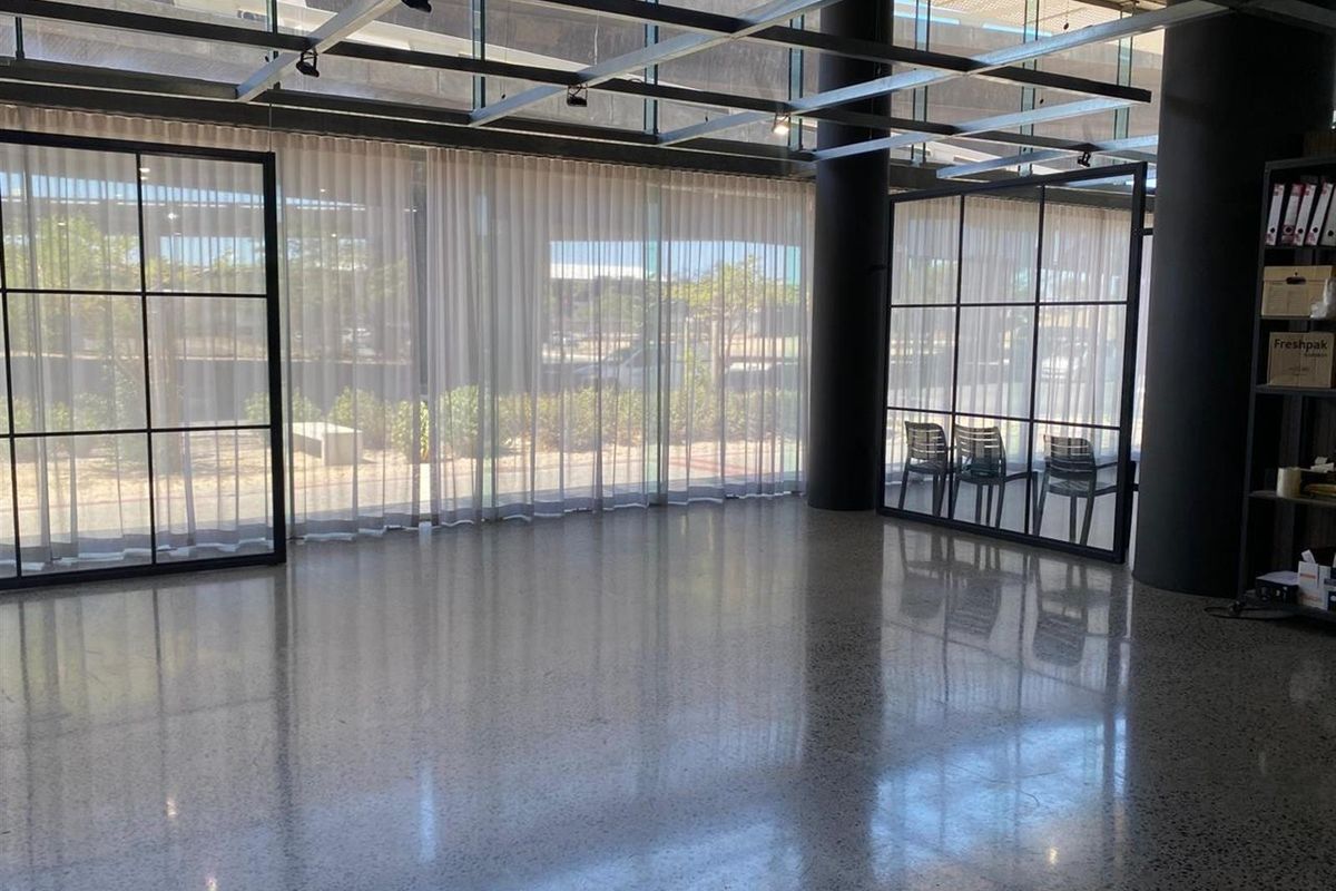 Modern open-plan retail space featuring polished concrete floors, floor-to-ceiling glass windows with black steel framing, and an exposed industrial-style ceiling grid.