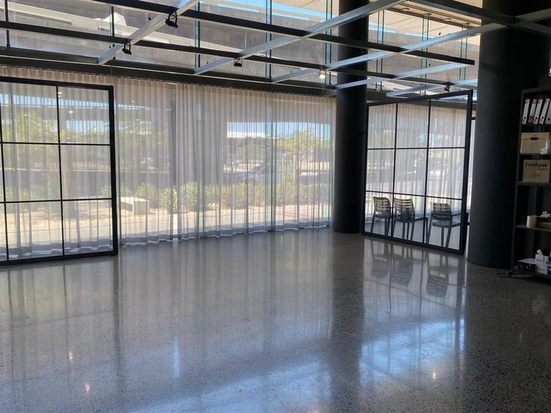 Modern open-plan retail space featuring polished concrete floors, floor-to-ceiling glass windows with black steel framing, and an exposed industrial-style ceiling grid.
