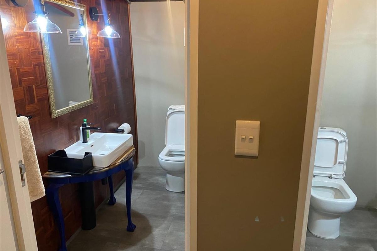 A functional bathroom space featuring a vanity basin, wall-mounted mirror, and two separate toilet cubicles with tiled flooring.