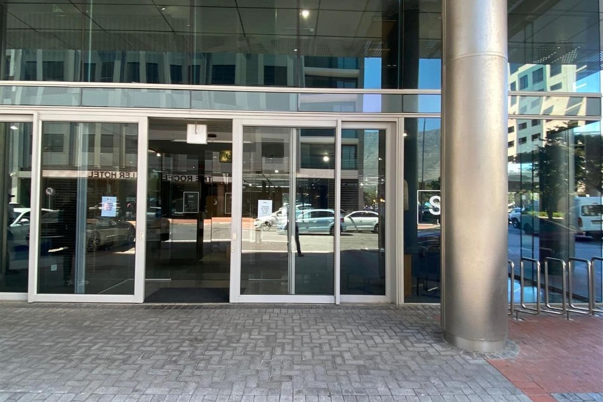 Modern commercial building entrance featuring large glass sliding doors, a sleek metal support column, and paved exterior access area.