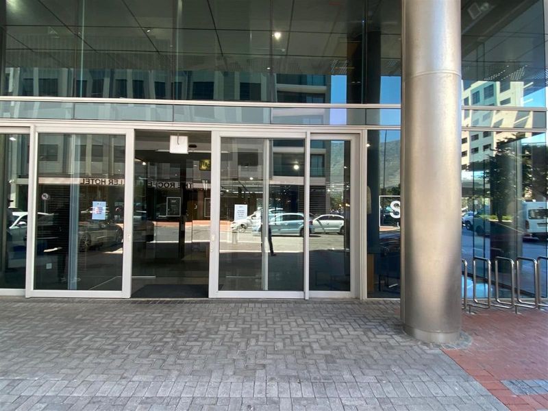 Modern commercial building entrance featuring large glass sliding doors, a sleek metal support column, and paved exterior access area.