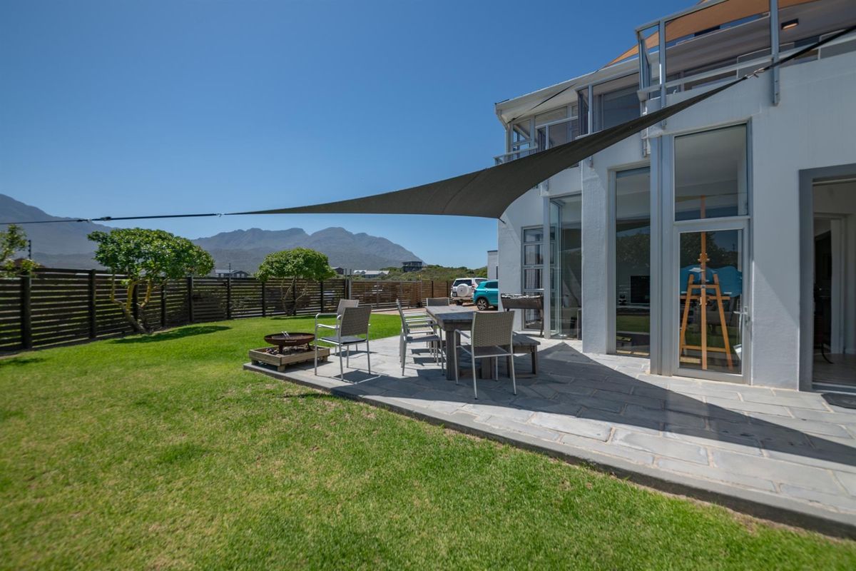 A spacious rear patio featuring stone paving, a shade sail, and direct access to the garden with mountain views.