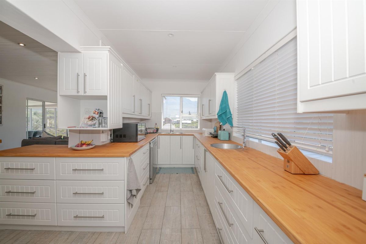 A bright, modern kitchen featuring white cabinetry, timber countertops, and tiled flooring, offering a clean and functional workspace.