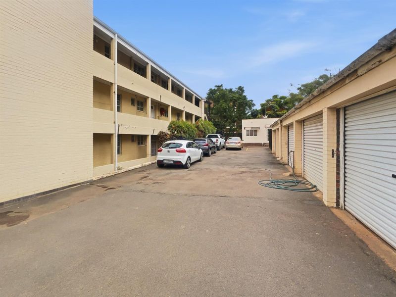 Exterior view of the apartment complex featuring a multi-level residential building, paved driveway, and a row of private lock-up garages.