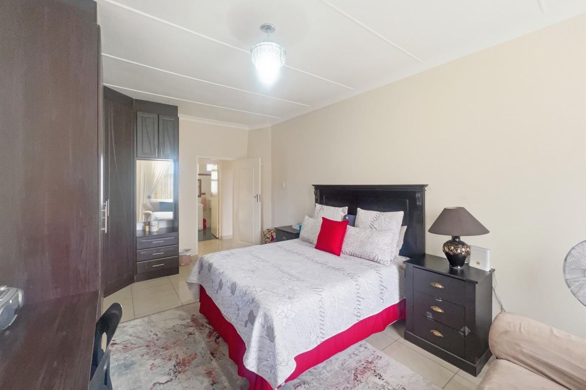 A bedroom featuring built-in dark wood cabinetry and tiled flooring, with an adjoining doorway leading to an en-suite bathroom.