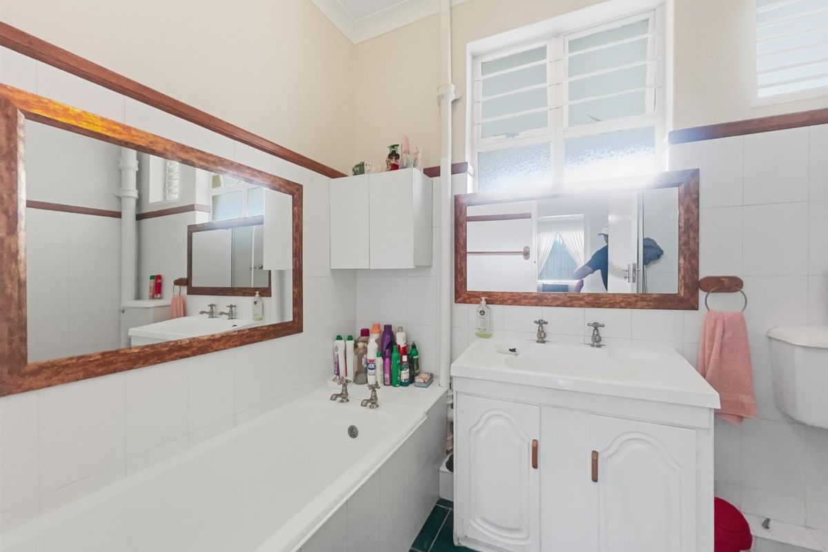 A functional bathroom featuring a built-in bathtub, vanity cabinet with integrated sink, wall-mounted mirrors, and tiled flooring.