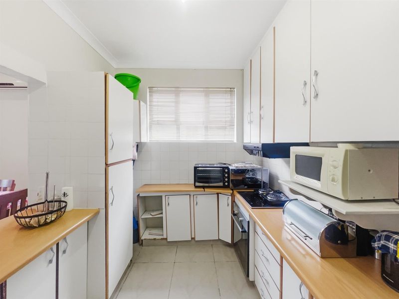 A functional galley-style kitchen featuring white cabinetry, tiled splashbacks, a built-in oven, and a cooktop with an extractor fan.