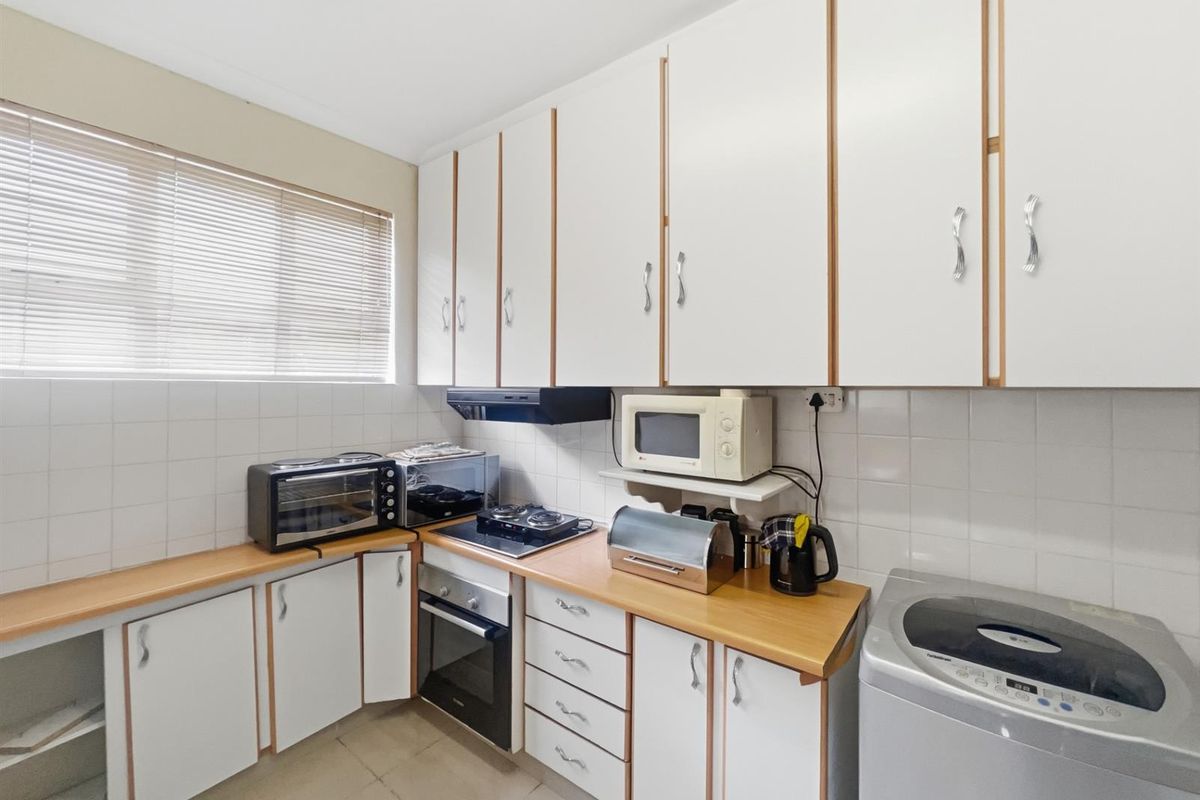 A functional kitchen featuring white cabinetry, wood-look countertops, a built-in oven, and a hob with an extractor fan.