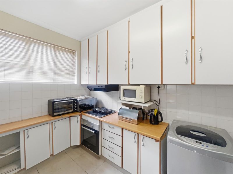 A functional kitchen featuring white cabinetry, wood-look countertops, a built-in oven, and a hob with an extractor fan.