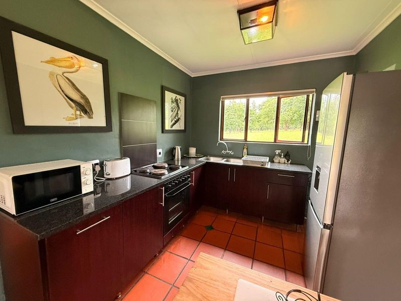 A functional kitchen featuring dark cabinetry, granite countertops, a built-in oven with hob, and terracotta floor tiles.