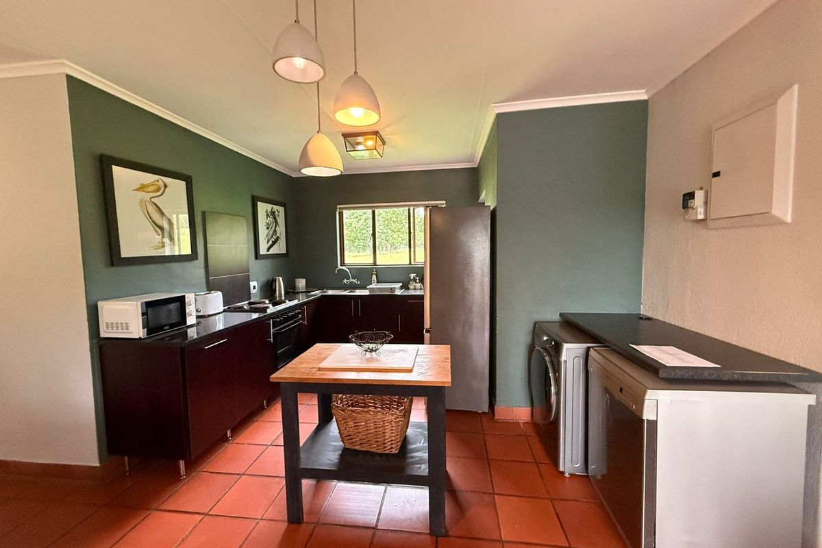 A functional kitchen featuring dark cabinetry, terracotta floor tiles, and a dedicated laundry area with built-in appliance connections.