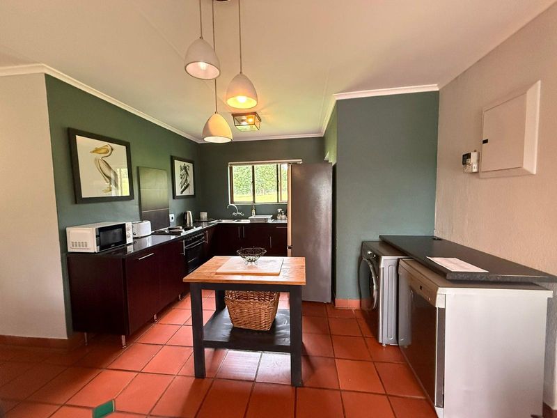A functional kitchen featuring dark cabinetry, terracotta floor tiles, and a dedicated laundry area with built-in appliance connections.