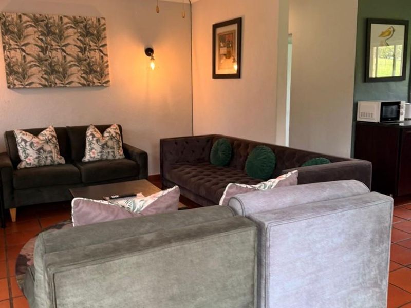 A comfortable living room featuring terracotta floor tiles, a ceiling fan, and wall-mounted lighting, creating a warm and inviting atmosphere.