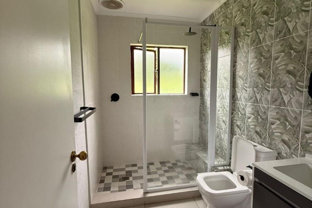 A modern bathroom featuring a glass-enclosed walk-in shower, patterned feature tiling, a wall-mounted vanity, and a toilet.