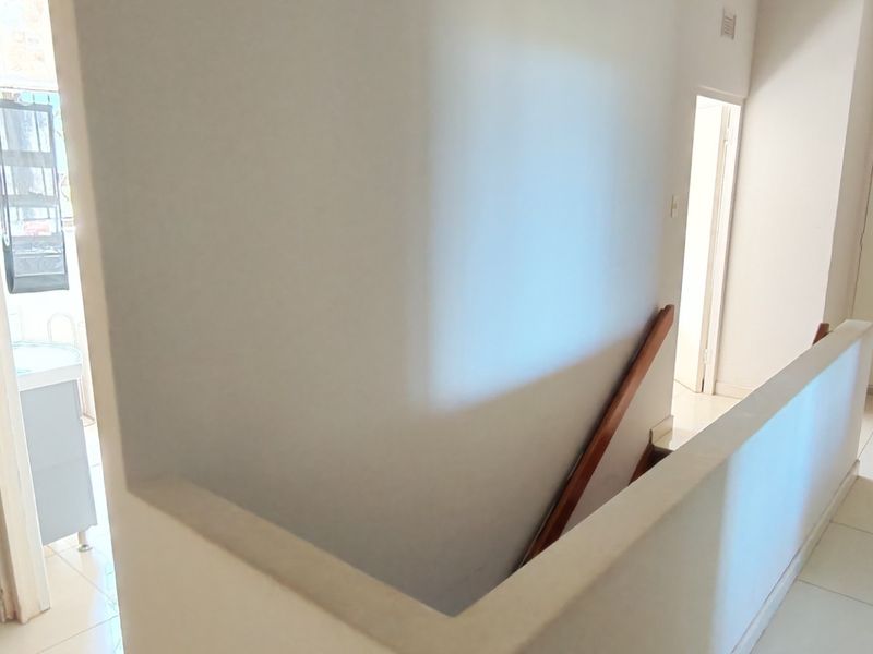 A bright upstairs hallway featuring tiled flooring, built-in storage cupboards, and a staircase with a wooden handrail leading to the lower level.
